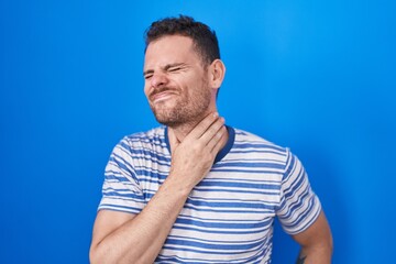 Fototapeta premium Young hispanic man standing over blue background touching painful neck, sore throat for flu, clod and infection