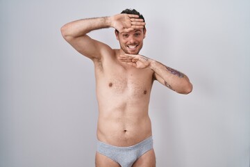 Fototapeta premium Young hispanic man standing shirtless wearing underware smiling cheerful playing peek a boo with hands showing face. surprised and exited