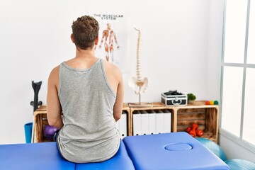 Young hispanic man on back view sitting on massage board at clinic