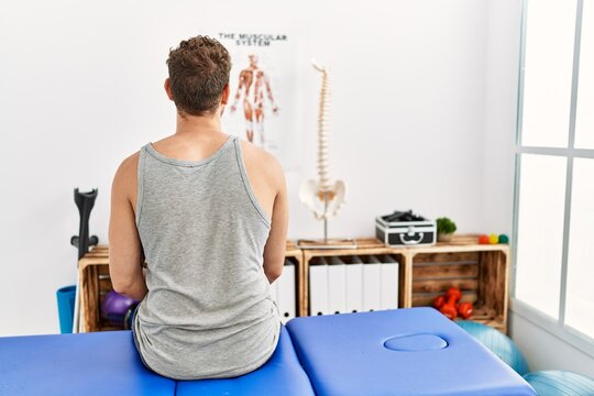 Young Hispanic Man On Back View Sitting On Massage Board At Clinic