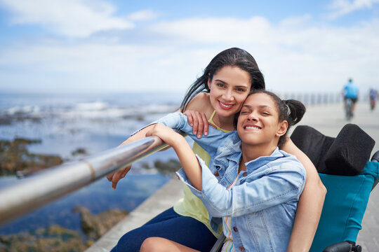 Portrait happy mother and disabled daughter at ocean railing