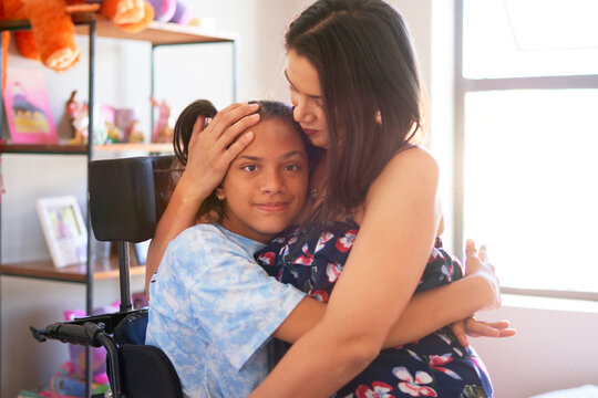 Portrait affectionate mother hugging disabled daughter at home
