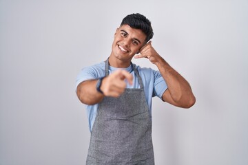 Hispanic young man wearing apron over white background smiling doing talking on the telephone...
