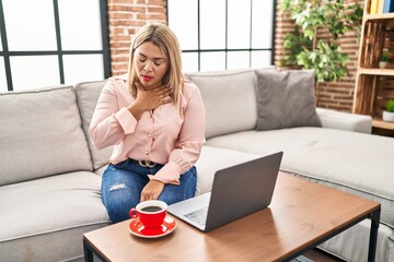 Young hispanic woman using laptop sitting on the sofa at home feeling unwell and coughing as...