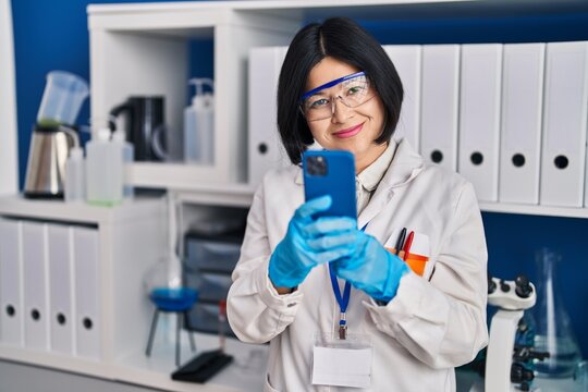 Young chinese woman scientist using smartphone working at laboratory
