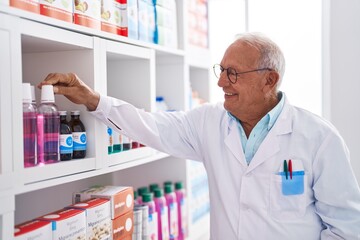 Senior grey-haired man pharmacist smiling confident organize shelving at pharmacy