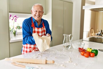 Senior man smiling confident holding dough with hands at kitchen