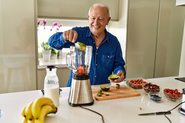Senior man smiling confident putting avocado in blender at kitchen