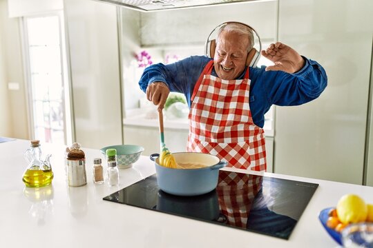 Senior man listening to music cooking spaghetti at kitchen