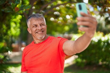 Naklejka na ściany i meble Middle age grey-haired man smiling confident making selfie by the smartphone at park