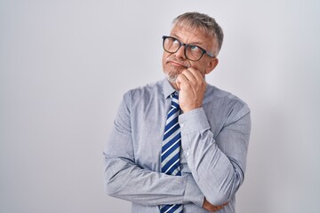 Hispanic business man with grey hair wearing glasses with hand on chin thinking about question,...