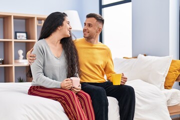 Man and woman couple drinking coffee sitting on bed at bedroom