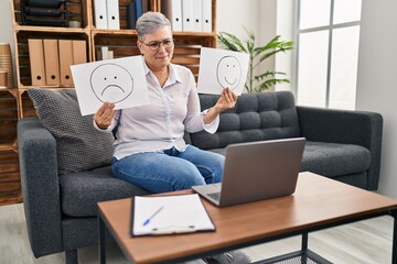 Middle age woman working on depression holding sad to happy emotion paper relaxed with serious expression on face. simple and natural looking at the camera.