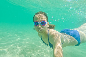 Naklejka premium Child girl swimming underwater with swim goggles. Dive and swimming in the sea. Have fun on summer vacation. 