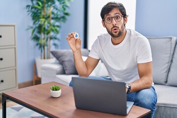 Handsome latin man holding virtual currency bitcoin using laptop scared and amazed with open mouth for surprise, disbelief face