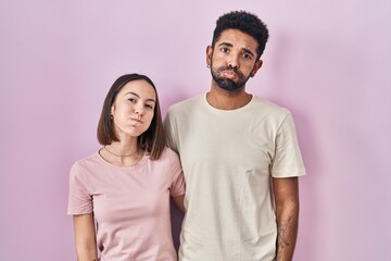 Obraz premium Young hispanic couple together over pink background puffing cheeks with funny face. mouth inflated with air, crazy expression.