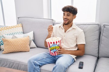 Fototapeta na wymiar Young arab man eating popcorn watching movie at home