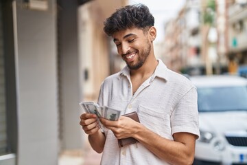 Young arab man smiling confident counting dollars at street