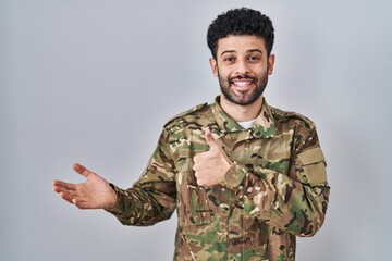Arab man wearing camouflage army uniform showing palm hand and doing ok gesture with thumbs up, smiling happy and cheerful
