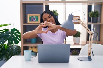 African american woman with braids using laptop at home smiling in love showing heart symbol and shape with hands. romantic concept.