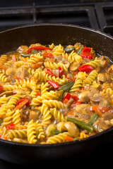 Pasta with vegetables in sauce and spices in a frying pan close-up.