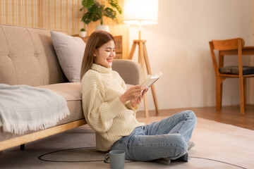 Young asian woman drinking coffee and reading a book while wearing sweater and sitting to relaxation