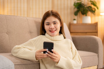 Young asian woman chatting with customer on smartphone and drinking coffee while wearing sweater and