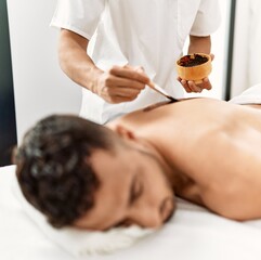 Two hispanic men physiotherapist and patient having skin back treatment using exfoliating lotion at beauty center