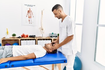 Two hispanic men physiotherapist and patient having rehab session massaging head at clinic