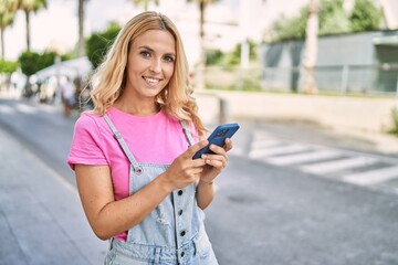 Young blonde woman smiling confident talking on the smartphone at street
