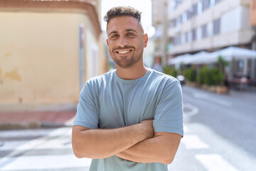 Young hispanic man standing with arms crossed gesture at street