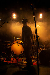 drummer in semi-shadow on scene of band, background lighting, smoke on stage