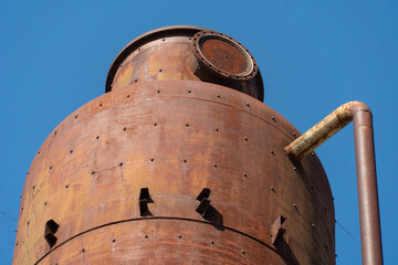 An old metal rusty water tower. Old production technology, processing, drying in the agro-industrial complex. Red silo on the sky background. Metal construction © Pokoman