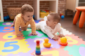 Two toddlers playing with toys sitting on floor at kindergarten