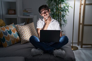 Young hispanic man using laptop at home at night touching painful neck, sore throat for flu, clod and infection