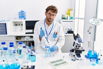 Fototapeta premium Young hispanic man wearing scientist uniform working at laboratory