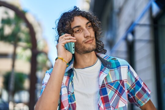 Young hispanic man talking on smartphone with serious expression at street