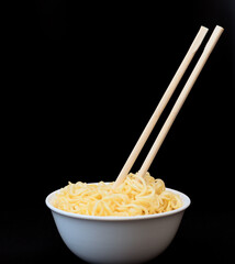 Instant Chinese curly noodles in white bowl with wood sticks on black background. Selective focus. Asian food concept. Unhealthy eating
