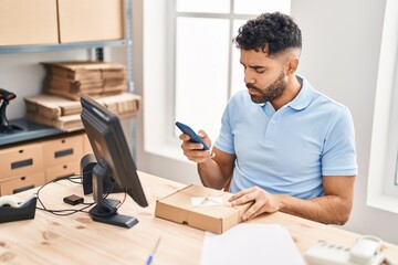 Fototapeta premium Young hispanic man ecommerce business worker using smartphone at office