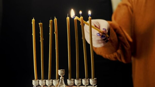 A woman's hand lights candles on the last day of Hanukkah from the shamash candle in the Hanukkah menorah. Medium plan