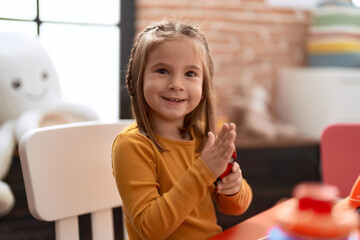 Adorable hispanic girl smiling confident sitting on table at kindergarten