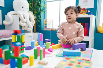 Adorable chinese girl playing with construction blocks standing at kindergarten