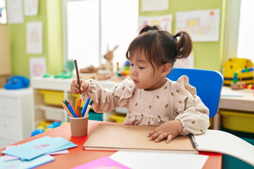 Adorable chinese girl preschool student sitting on table drawing on notebook at kindergarten