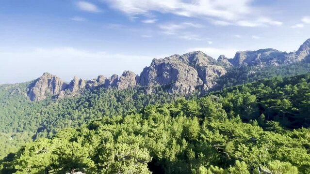 Very rocky Corsican mountain range of the Aiguilles de Bavella in summer, very tall and wide massif of France, near Zonza in Conca forest, with some trees in bottom, right rotation movement