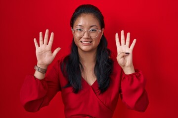 Asian young woman standing over red background showing and pointing up with fingers number nine...