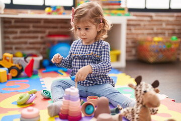 Adorable hispanic girl playing with hoops game sitting on floor at kindergarten