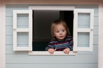 boy watching from window. wooden toy house. kid looks out, Portrait toddler, interesting emotions