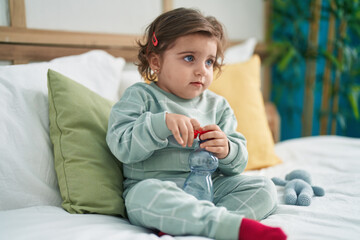 Adorable hispanic girl sitting on bed with holding water bottle at bedroom