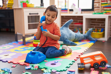 Adorable hispanic toddler smiling confident sitting on floor playing with telephone toy at kindergarten