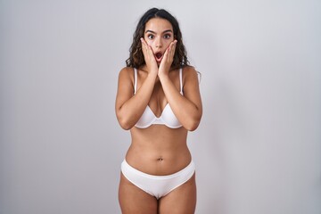 Young hispanic woman wearing white lingerie afraid and shocked, surprise and amazed expression with hands on face